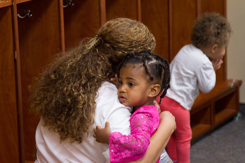 A staff member greets a toddler in a nonverbal way