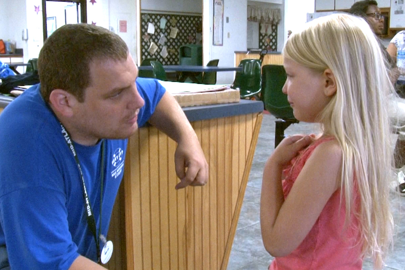 A caregiver kneels to talk with a crying child